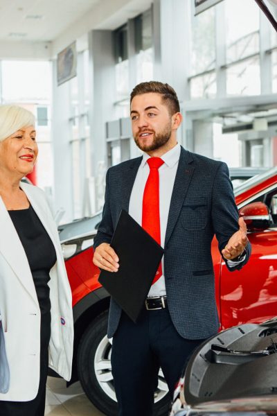 Aged couple look  new car with dealer in car showroom.